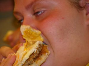 Foto de Byron Solomon mostrando uma pessoa obesa comendo um hambúrguer. Obesidade